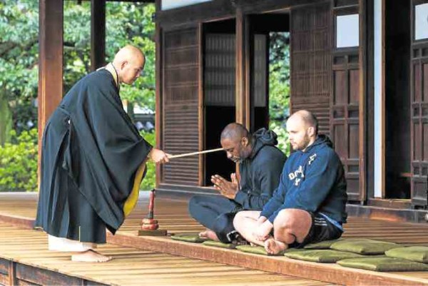 A monk performs a rite with Elba (center) and trainer Kieran Keddle.