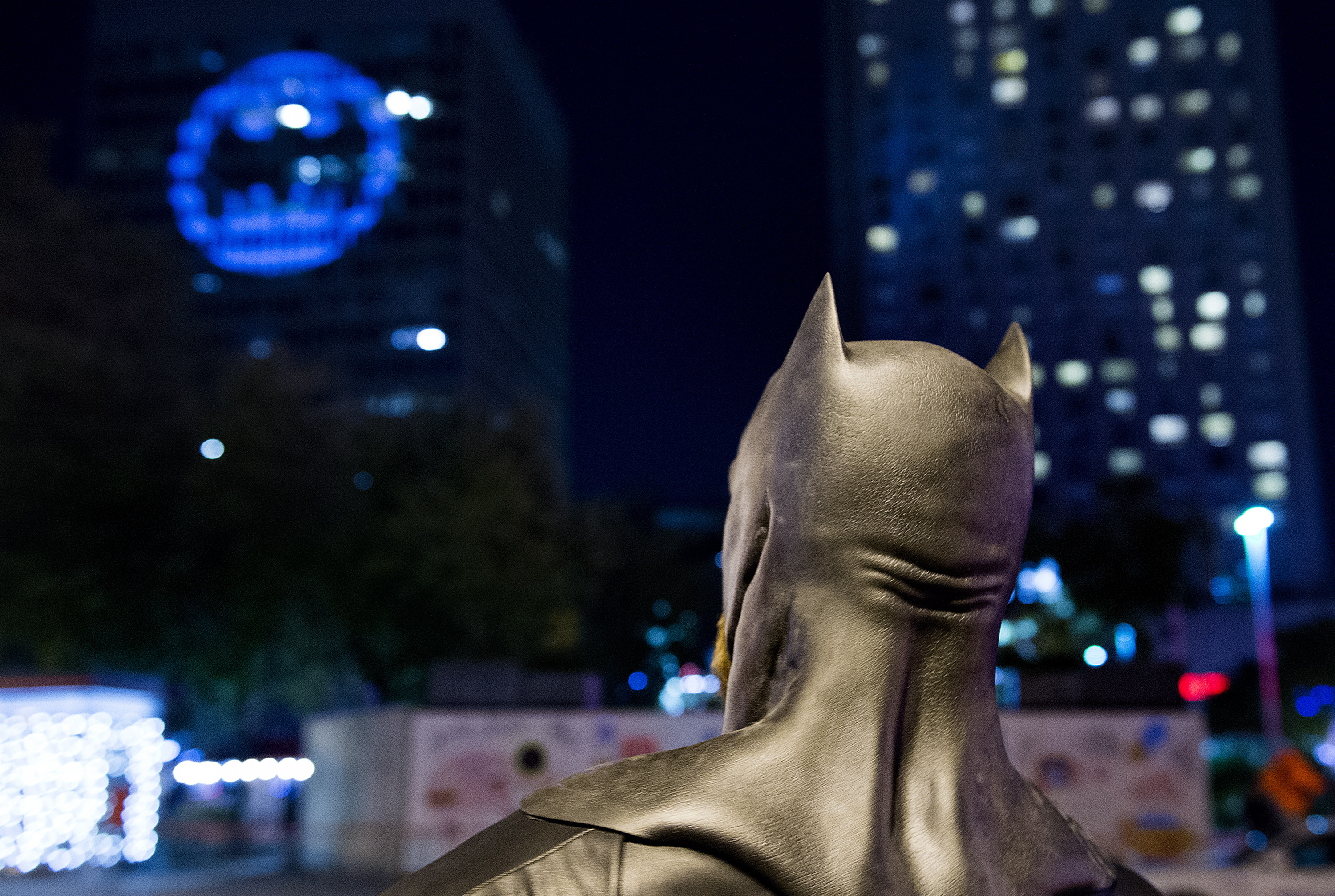 A man dressed as Batman looks up towards the Batman signal projected onto a building to celebrate Batman Day in Montreal, Saturday, Sept. 21, 2019. The night sky all over the world is lighting up Saturday with an illumination of the famed bat insignia to mark a special anniversary for Batman. DC Comics is carrying off a celebration of Batman Day to mark the 80th anniversary of the appearance of crimefighter Bruce Wayne and his masked hidden identity. (Graham Hughes/The Canadian Press via AP)