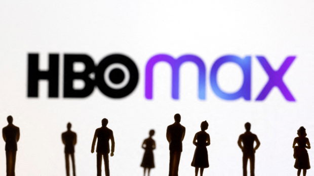 Toy figures of people are seen in front of the displayed HBO Max logo, in this illustration