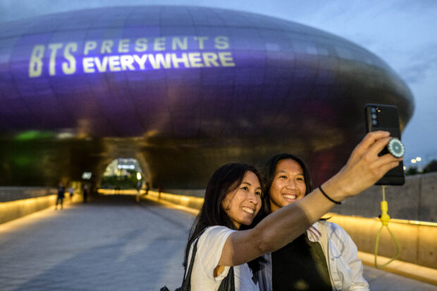 A mother and her daughter take a selfie in front of the Dongdaemun Design Plaza as it is illuminated in purple light to mark the 10-year anniversary of K-pop megastars BTS, in Seoul on June 12, 2023. Fans of K-pop megastars BTS flocked to hotspots around Seoul on June 12 to mark the supergroup's 10-year anniversary, with South Korea unveiling a special commemorative stamp series to celebrate. (Photo by ANTHONY WALLACE / AFP)