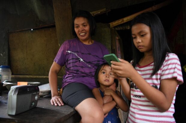 This photo taken on October 4, 2023 shows housewife Cristiteta Arpon listening to a radio drama with her children outside their house at a village in Silang, Cavite province. Radio dramas were the main source of entertainment for Filipino families after World War II, just like the rest of the world, but their popularity faded with the rise of television, social media and video live-streaming. (Photo by Ted ALJIBE / AFP) / To go with AFP story Philippines-entertainment-radio, FOCUS by Cecil MORELLA