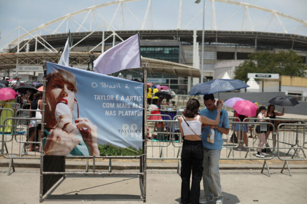 A couple protect themselves with an umbrella for high temperatures, as they wait before the Taylor Swift concert, following the death of a fan due to the heat during the first day concert, in Rio de Janeiro, Brazil, Nov. 18, 2023. 