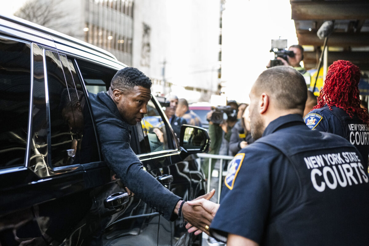 Jonathan Majors shakes hands with court police officers 